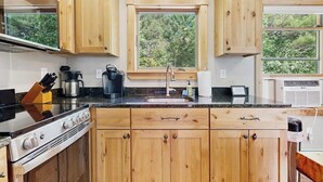 Une cuisine avec des meubles en bois, une cuisinière, un évier et une fenêtre donnant sur les arbres.