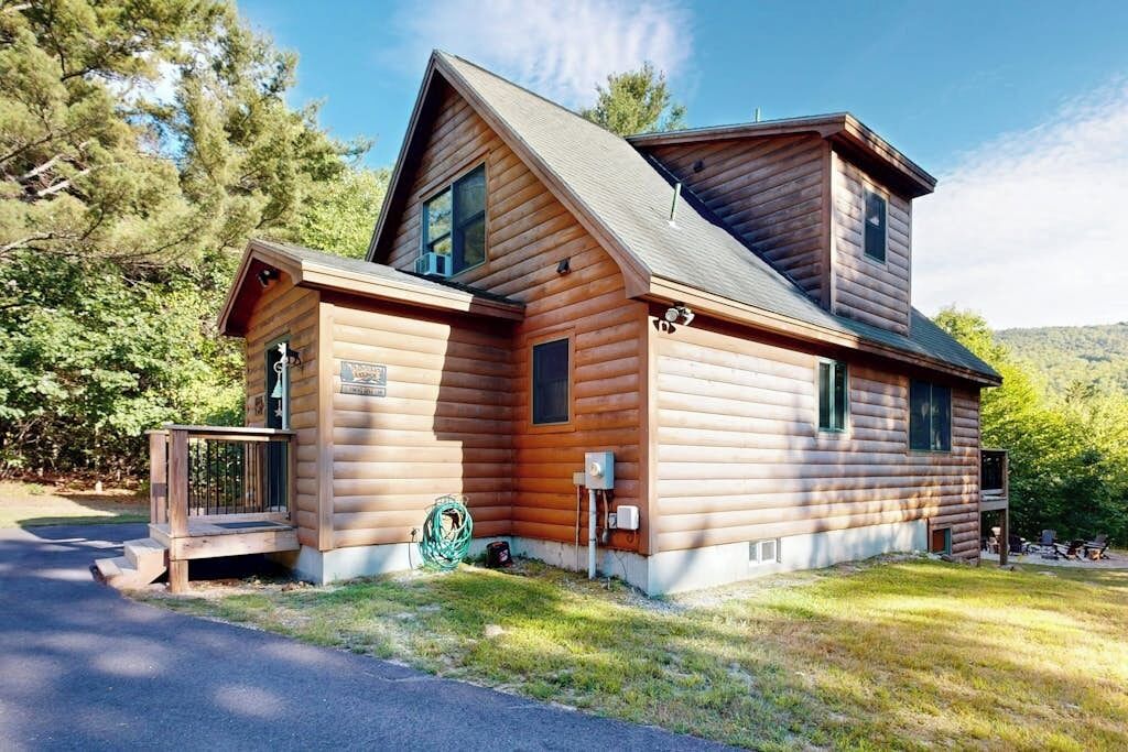 A log cabin with a porch, a chimney, and a small deck.