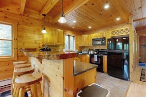 Ein Holzblockhaus-Interieur mit einer Küche, die eine zentrale Kochinsel, Barhocker, eine Mikrowelle und einen Kühlschrank umfasst.