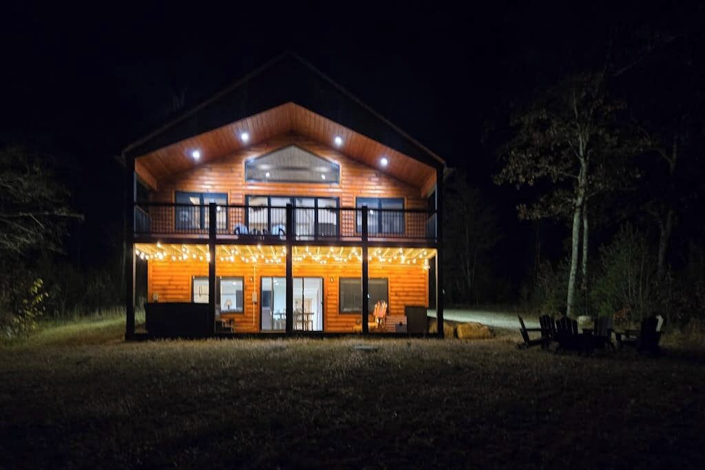 Eine zweistöckige Holzhütte mit Balkon, großen Fenstern und einer Veranda.
