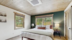 A bedroom with a bed, two windows, a nightstand, and a lamp. - Spacious mountain retreat with fire pit, hot tub, sauna, and foosball (Bethel)