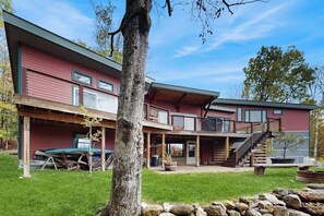 Ein zweigeschossiges Gebäude mit überdachter Terrasse, einer Treppe und einem Baum im Vordergrund.