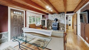 A wooden interior with a glass table, a stone fireplace, and a door leading to another room. - Spacious Mountain Chalet with Sauna, Deck, and Ski/Snowboard Adventures Nearby (Bethel)