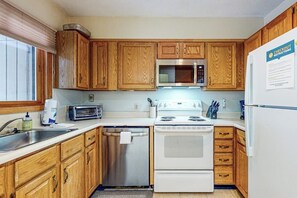 A kitchen with wooden cabinets, a microwave, a stove, and a refrigerator. - Dog-Friendly Slopeside Condo - Walk to Slopes - Fireplace, Firepit & WiFi (Newry)