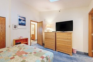 A bedroom with a bed, a television on a dresser, a lamp, and a door leading to another room. - Dog-Friendly Slopeside Condo - Walk to Slopes - Fireplace, Firepit & WiFi (Newry)