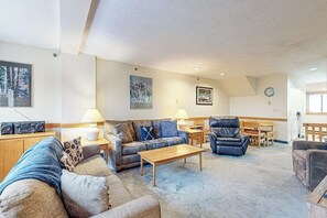 A living room with a sofa, armchair, coffee table, and a dining area with a table and chairs. - Dog-Friendly Slopeside Condo - Walk to Slopes - Fireplace, Firepit & WiFi (Newry)