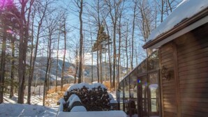 Eine Holzhütte mit Glastür, umgeben von verschneitem Gelände und Bäumen.