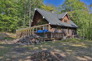 A cabin with a large deck, a covered porch, and a chimney.