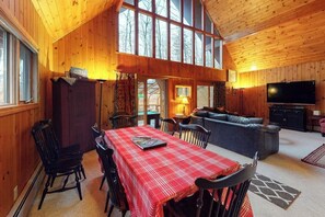 A wooden interior with a dining table, chairs, a sofa, and a TV.