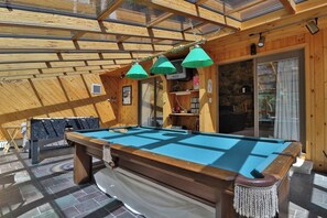 A pool table in a wooden room with a glass ceiling, a stone wall, and a door leading outside.