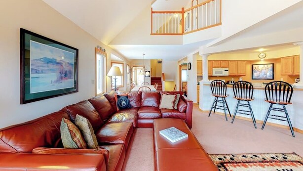A spacious living area with a large leather sofa, a dining table, and a kitchen in the background. - Cute townhome on the slopes with trail access, deck, hot tub & pool (Newry)