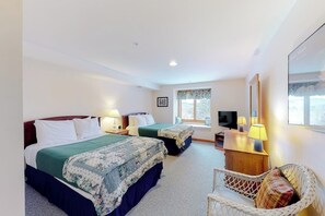 A hotel room with two beds, a television, a desk with a lamp, a wicker chair, and a window with a view. - Locke Mountain ski-in/ski-out townhome with trail access to White Cap (Newry)