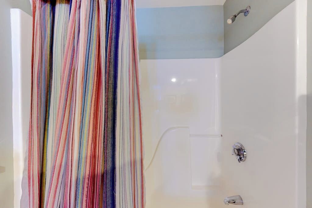 Eine Dusche mit weißer Wand und bunter Duschvorhang.
