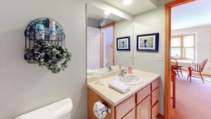 A bathroom with a white sink, mirror, and wooden cabinets. - Cute townhome on the slopes with trail access, deck, hot tub & pool (Newry)