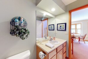 A bathroom with a white sink, mirror, and wooden cabinets. - Cute townhome on the slopes with trail access, deck, hot tub & pool (Newry)