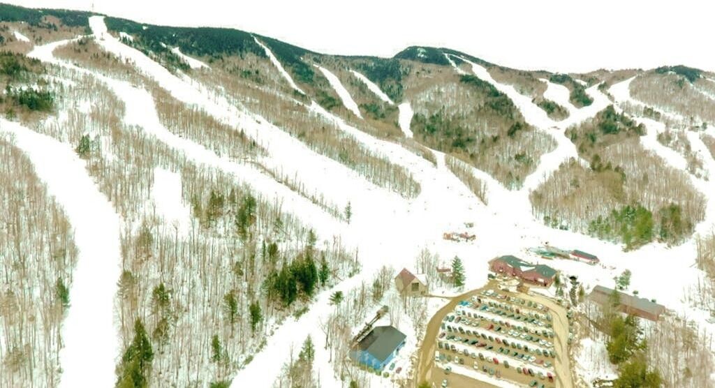 An aerial view of a ski resort with a parking lot, buildings, and a ski lift.