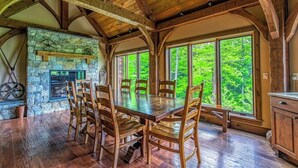 A dining area with a stone fireplace, wooden beams, and large windows overlooking greenery. - Stunning mountain-view estate with private pool & hot tub - near slopes (Newry)