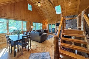 Ein Holzblock-Interieur mit Essbereich, Wohnzimmer und einer Treppe, die zu einem Schlafraum im Obergeschoss führt.