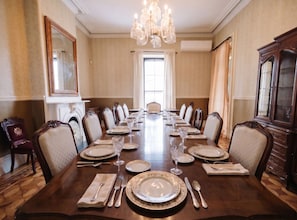 Un comedor formal con una larga mesa dispuesta para una comida, sillas elegantes, un candelabro y un espejo grande.