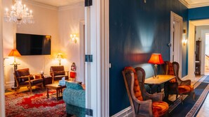 A living room with a TV, two chairs, a table, a chandelier, and a red carpet. - The Hillard - A Private Historic Estate 1865 (Wilkes-Barre)