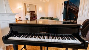 A grand piano in a spacious room with a chandelier, a staircase, and a view of a library. - The Hillard - A Private Historic Estate 1865 (Wilkes-Barre)