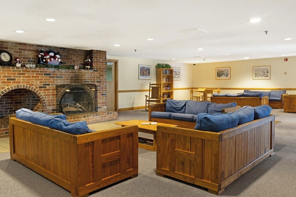 A cozy lounge area with a brick fireplace, wooden furniture, and a bookshelf.