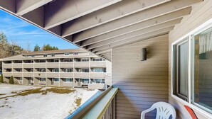 A balcony with a white plastic chair, a view of a multi-story building, and a snow-covered ground. - Ski-in/ski-out condo with shared pool & hot tub - steps away from ski lift (Newry)