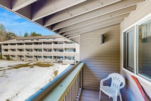 A balcony with a white plastic chair, a view of a multi-story building, and a snow-covered ground. - Ski-in/ski-out condo with shared pool & hot tub - steps away from ski lift (Newry)
