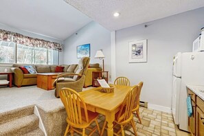 Un salon comprenant un canapé, des fauteuils, une table à manger avec des chaises, une lampe et un réfrigérateur.