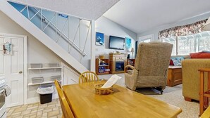 A dining area with a wooden table, chairs, a basket, and a staircase with a railing. - Ski-in/ski-out condo with shared pool & hot tub - steps away from ski lift (Newry)