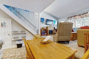 A dining area with a wooden table, chairs, a basket, and a staircase with a railing. - Ski-in/ski-out condo with shared pool & hot tub - steps away from ski lift (Newry)