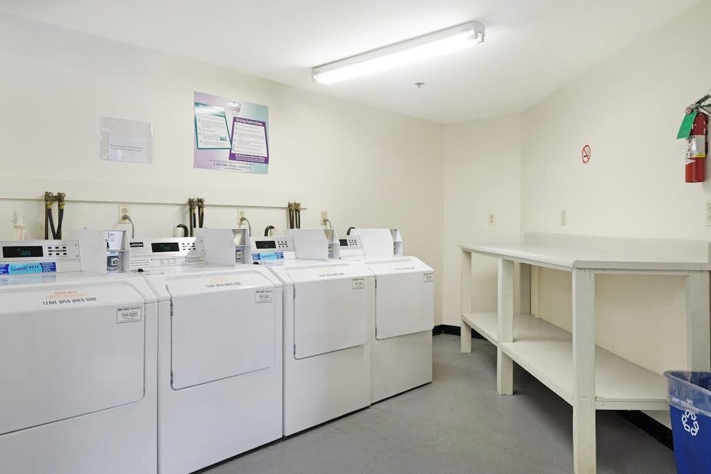 A laundry facility with multiple washing machines, a white table, and a fire extinguisher on the wall.