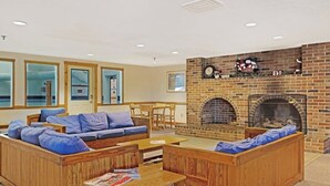 A living room with a brick fireplace, wooden furniture, and a dining area. - Ski-in/ski-out condo with shared pool & hot tub - steps away from ski lift (Newry)