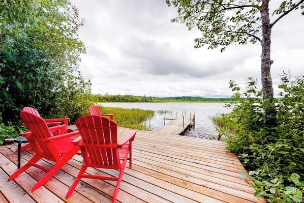 Una terraza de madera con sillas Adirondack rojas que dan a un lago.