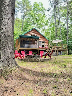 Eine Hütte mit Veranda, roten Stühlen und einem Kamin aus Stein.
