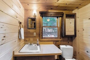 Un baño rústico con cabaña, que incluye un lavamanos, inodoro y ventana con vistas al exterior.