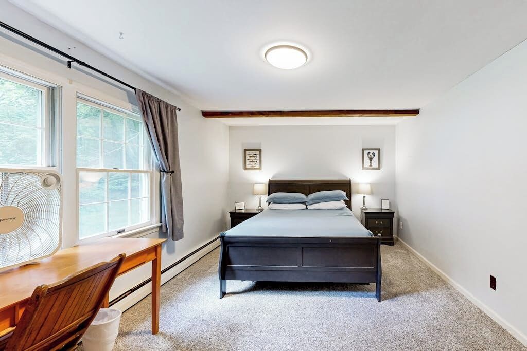 A bedroom with a bed, bedside tables, a desk, a chair, a window with curtains, and a ceiling fan.
