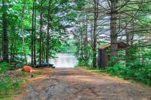 A forested area with a dirt path leading to a small wooden structure by a lake.