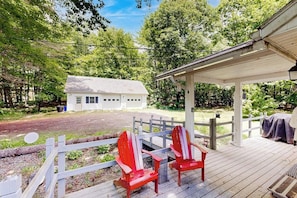 A wooden deck with Adirondack chairs, a covered area, and a white building in the background.