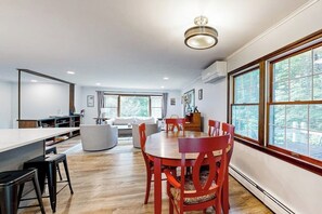 A modern kitchen with a dining area, large windows, and a ceiling light fixture.