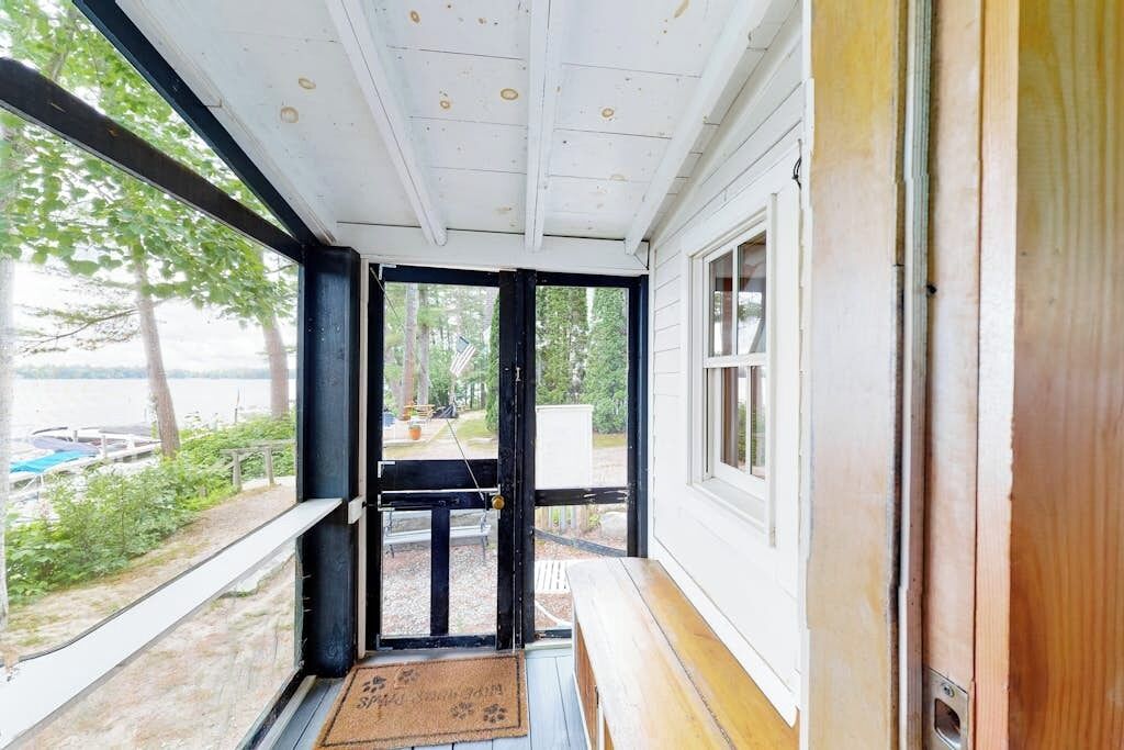 Un porche cubierto con vistas a un muelle y árboles, una puerta que da al exterior y un banco de madera.