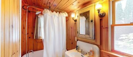 Ein Badezimmer einer Holzhütte mit Badewanne, Waschbecken, Spiegel und Fenster.