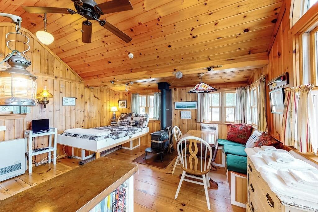 A cabin interior with a bed, seating area, dining table, and a fireplace.