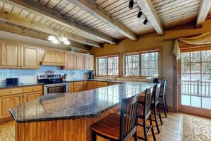 A kitchen with wooden cabinets, a granite countertop, and a large island with bar stools. - Expansive Retreat Near the Slopes with Media Room, Two Kitchens, Stone Fireplace (Newry)