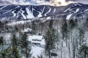 A snow-covered house surrounded by trees and mountains. - Expansive Retreat Near the Slopes with Media Room, Two Kitchens, Stone Fireplace (Newry)