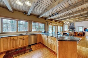 A spacious kitchen with wooden cabinets, a large island, and a stone fireplace. - Expansive Retreat Near the Slopes with Media Room, Two Kitchens, Stone Fireplace (Newry)