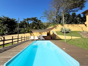 Ein rechteckiger Pool mit einer Holzterrasse, umgeben von einem Zaun und beschattet durch ein Sonnensegel.