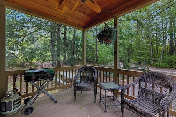 Eine überdachte Veranda mit Korbmöbeln, einem Grill und einem hängenden Blumentopf.