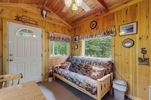 Ein Holzblockhaus-Interieur mit einer Couch, einem Esstisch, einem Fenster mit Vorhängen und einer Tür mit der Aufschrift 'Lodge'.