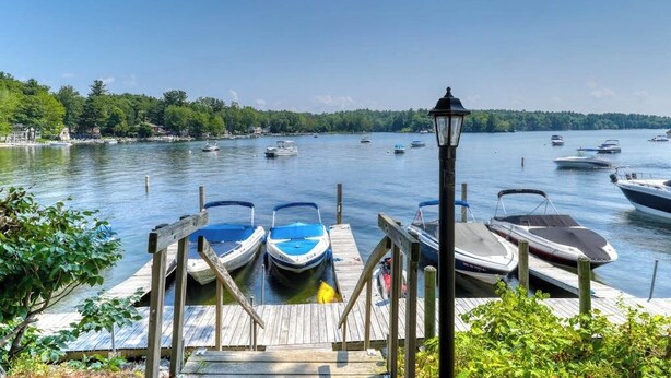 A wooden dock with boats, a lamp post, and a calm lake with boats. - Dog-Friendly Lakefront Cottage w/Lake Access, Deck, Gas Grill, A/C (Standish)